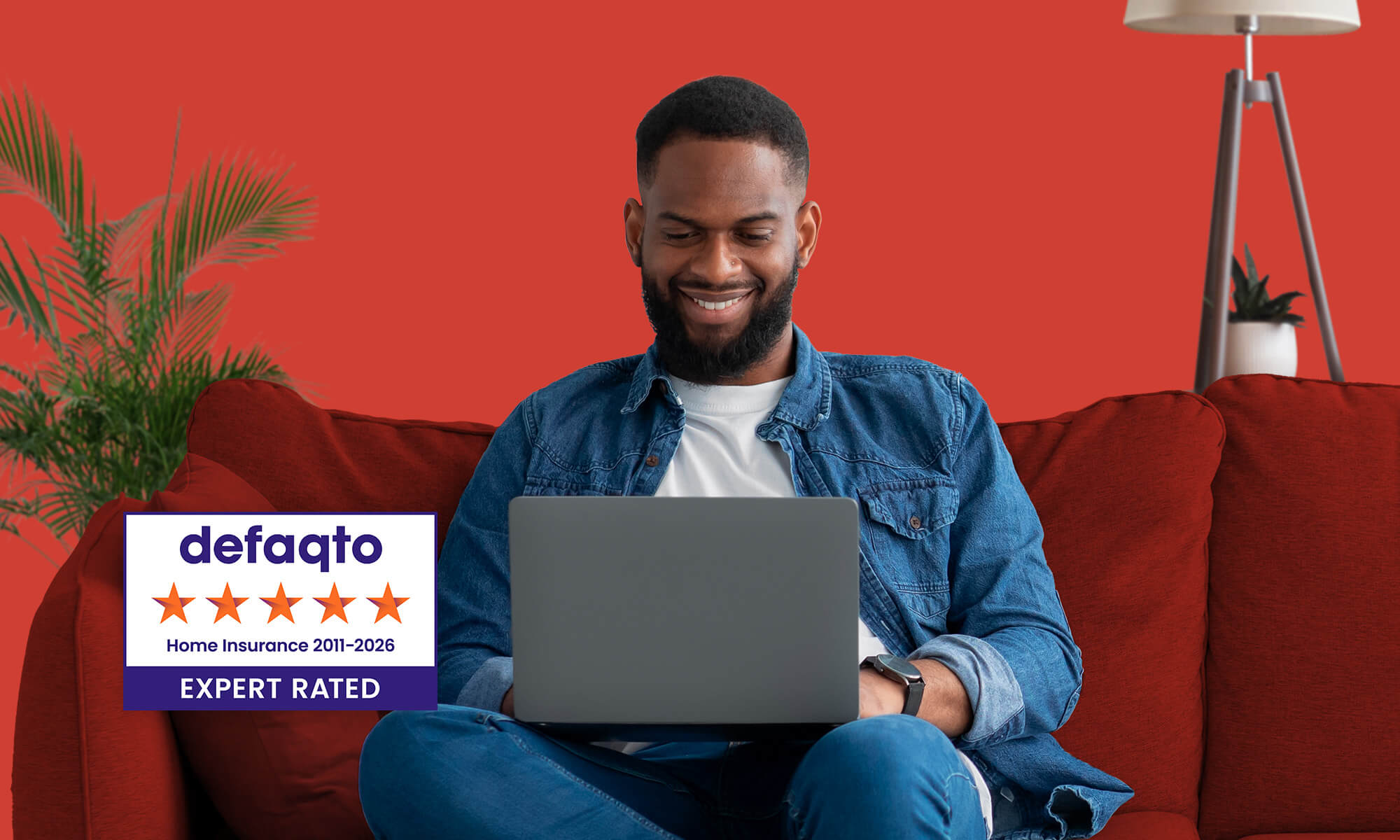 Man sits on red sofa with laptop and red background