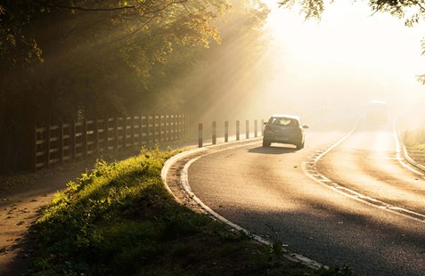 A grey car driving down a countryside sunny road