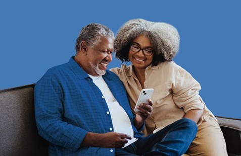 Couple sit on sofa with laptop against blue background