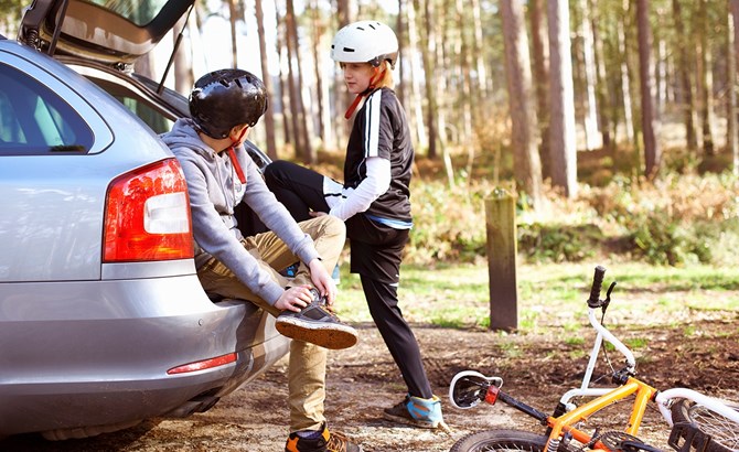 Two boys sat at the back of a car with a bike and helmets on