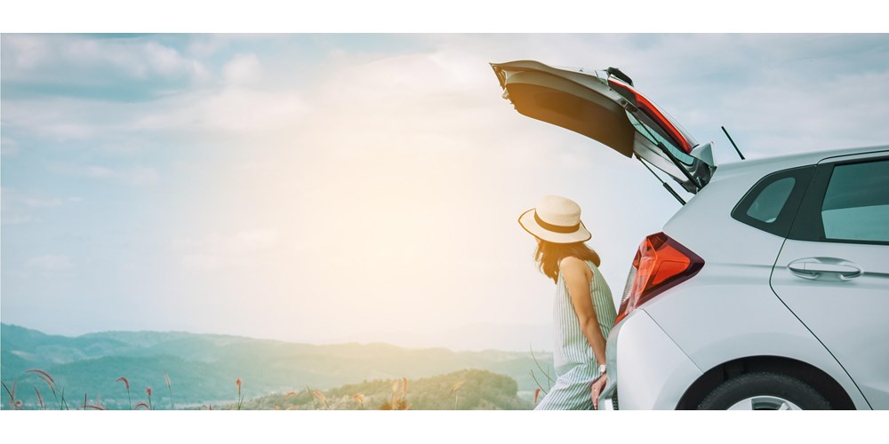 A woman sat at the boot of her car looking at the view