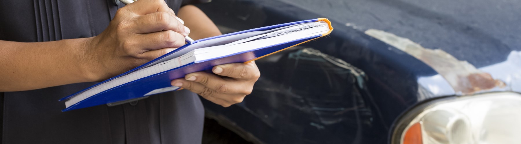 Man filling out form next to a damaged car