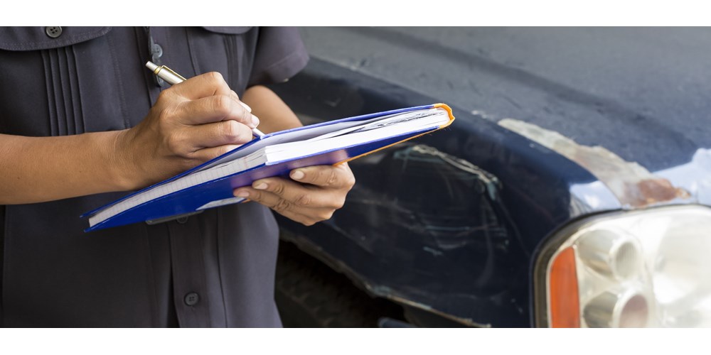 Man filling out form next to a damaged car