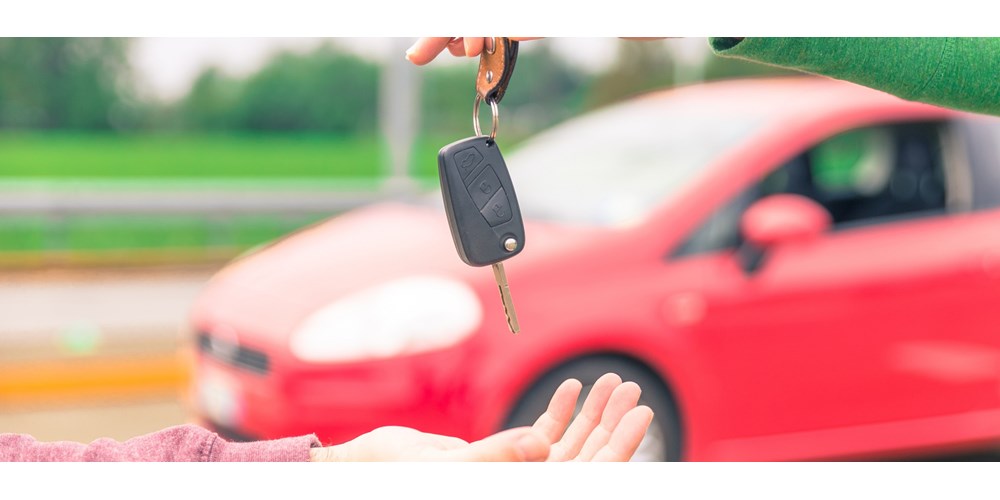 Car keys being delivered in front of red car