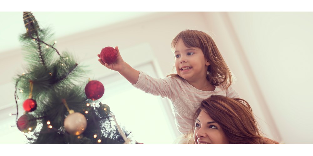 Mother with daughter on shoulders decorating a christmas tree