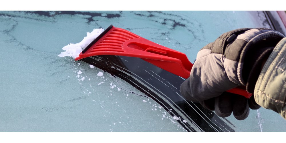 Red ice scraper scraping ice on car windscreen