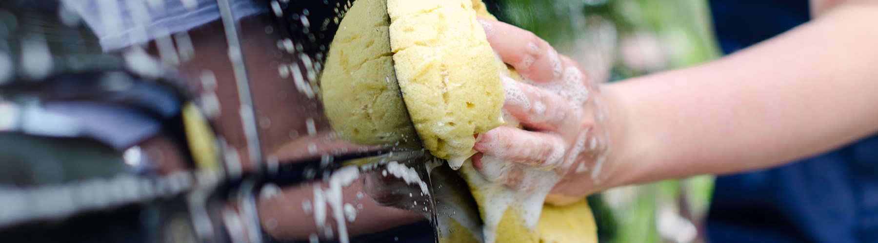 Woman's hand washing car with a yellow sponge
