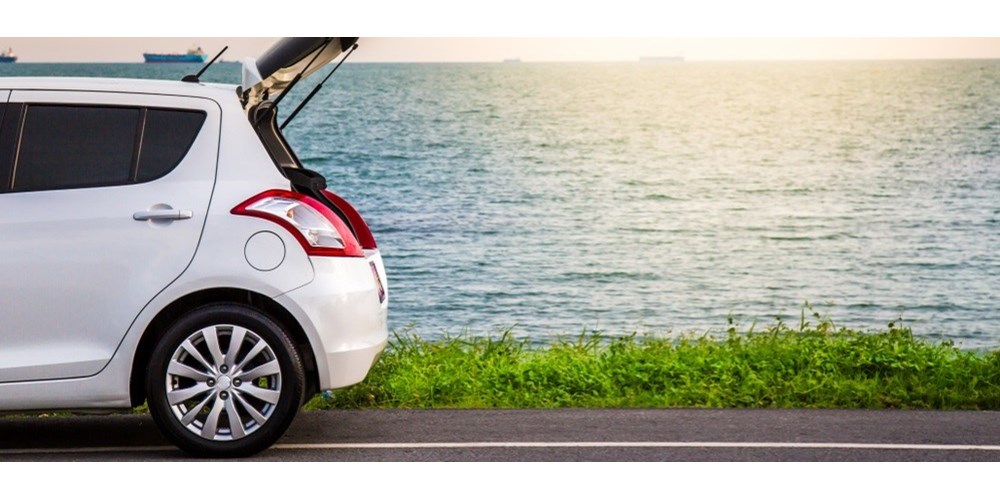 White hatchback car parked on a beach road with boot open