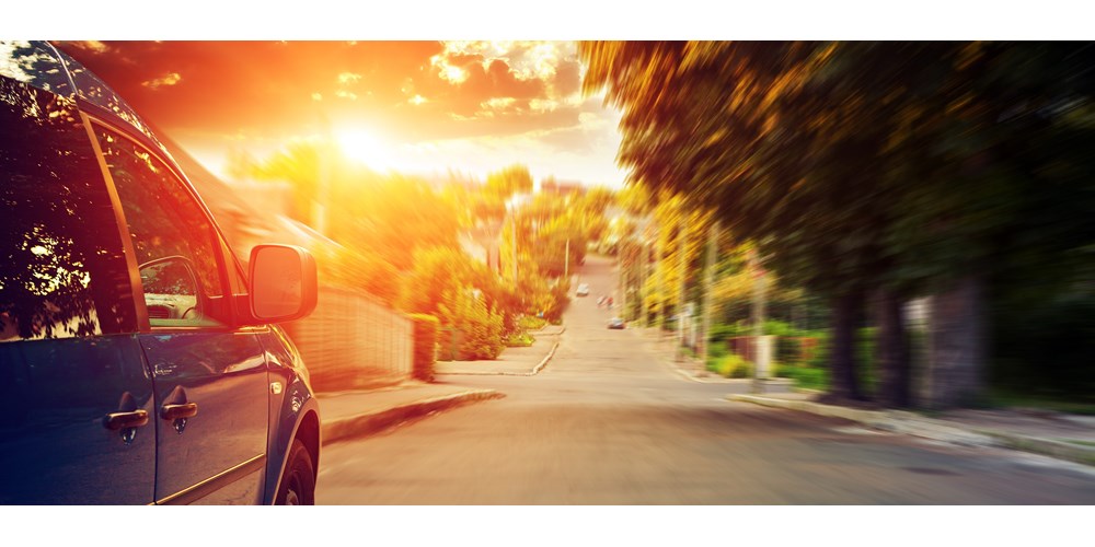 A blue car driving down a road towards the sunset