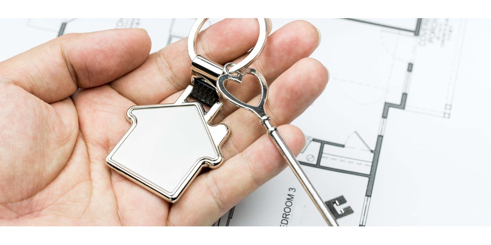 Hand holding a silver key with a house key ring