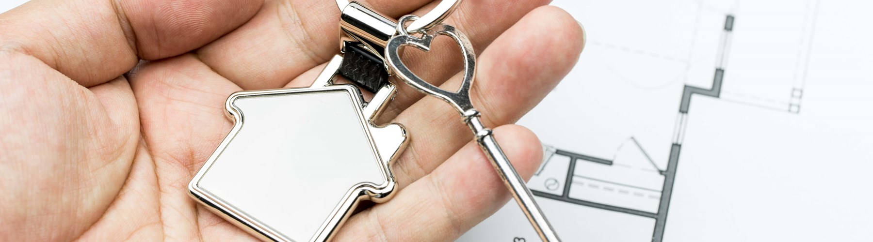 Hand holding a silver key with a house key ring