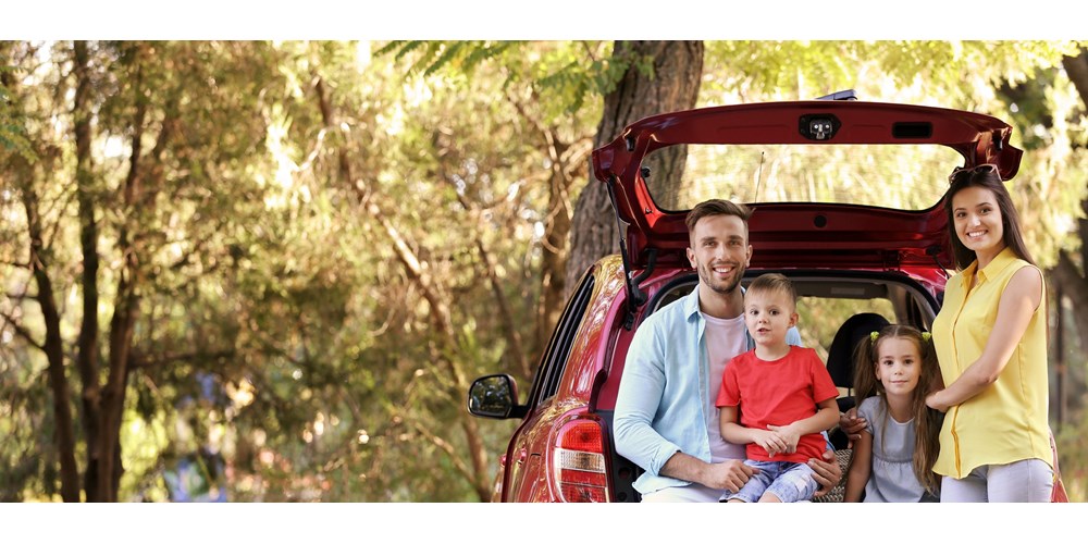 Family of four standing by a red car