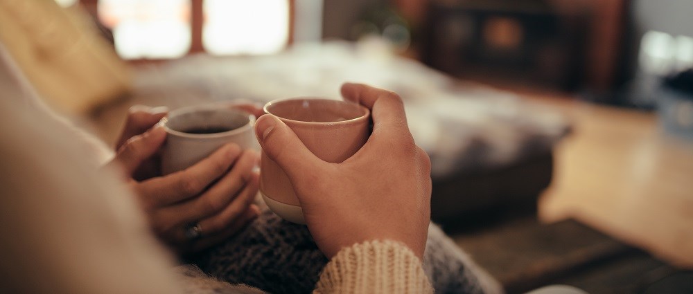 Couple holding mugs in front of fireplace
