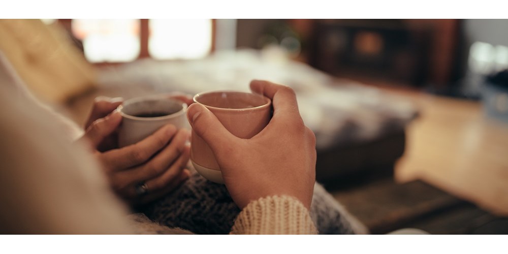 Couple holding mugs in front of fireplace