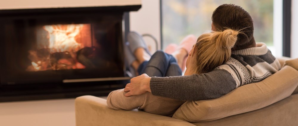 Couple sitting on sofa in front of fire. 
