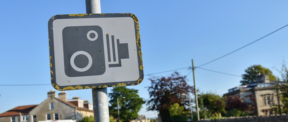 A speed camera road sign with moss