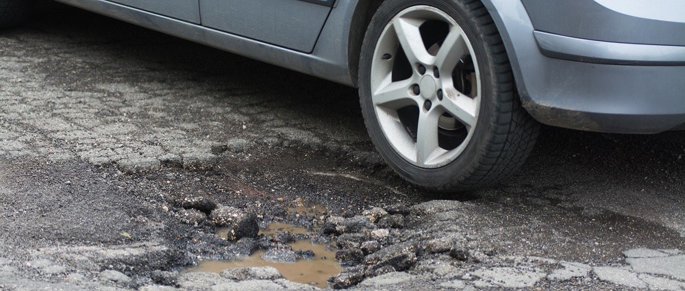Silver car next to pothole