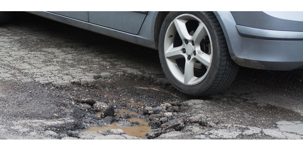 Silver car next to pothole