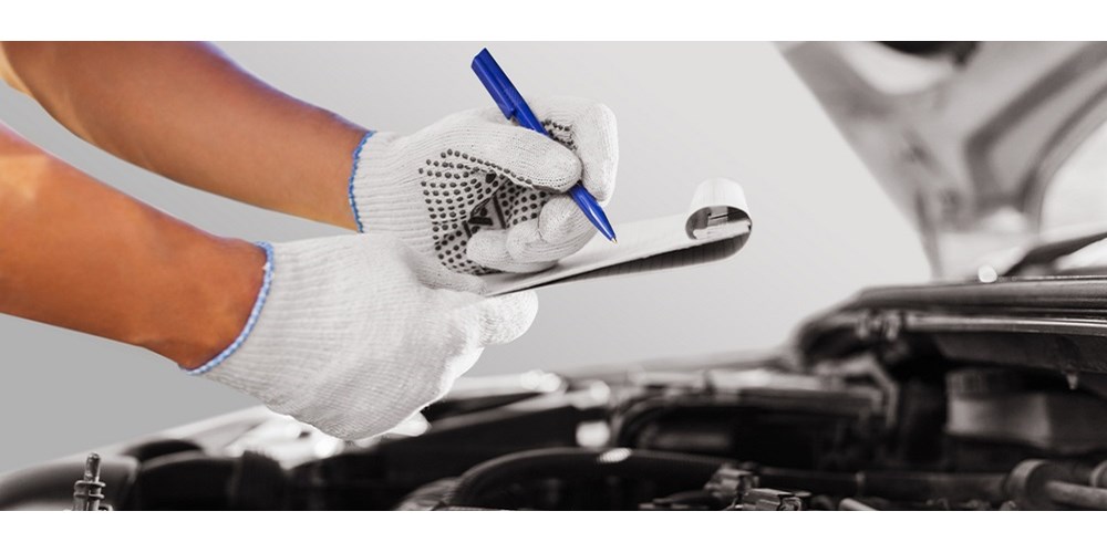 Someone making notes on a clipboard over a car engine 