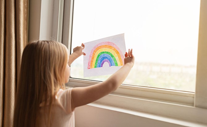 Child holding rainbow drawing at a window