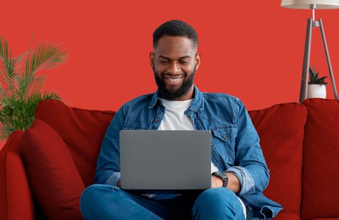 Man sits on red sofa with laptop and red background